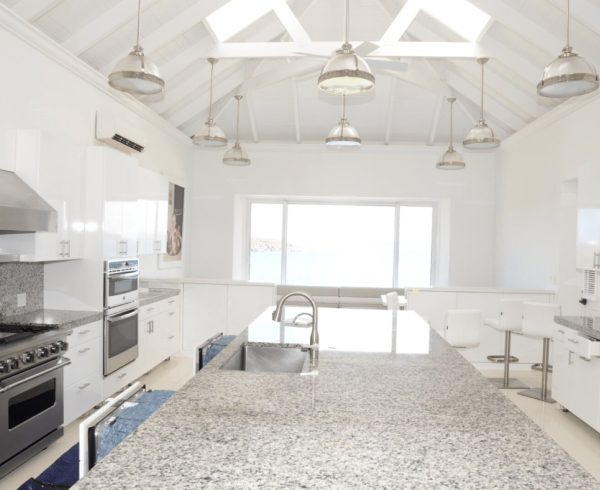 Modern white kitchen with a large granite-topped island, integrated sink and bar stools