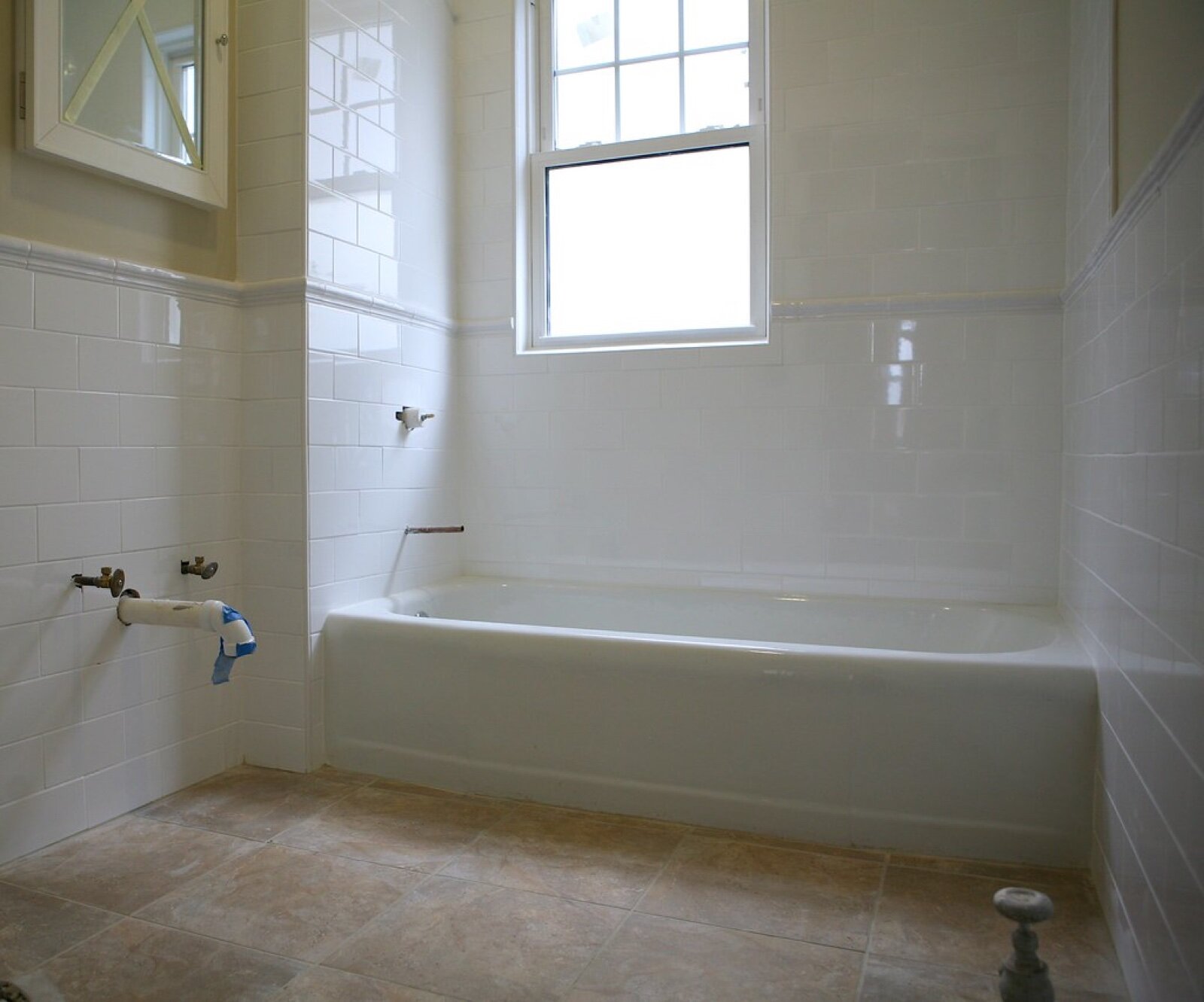 A tiled and grouted bathroom awaiting second fix, with capped pipes where the taps will go