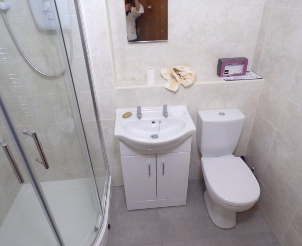 Small UK bathroom with a quadrant shower enclosure, wall-mounted shower unit, basin and toilet
