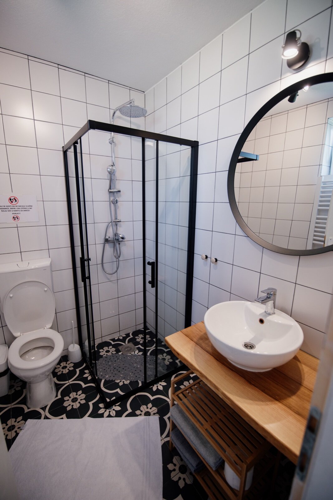 A small bathroom with a corner shower enclosure, round mirror and wall-hung basin