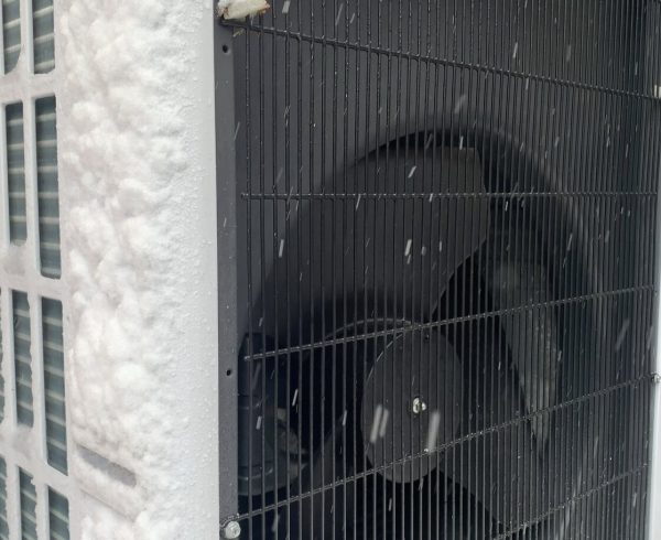 Air source heat pump outdoor unit running in falling snow against a brick wall