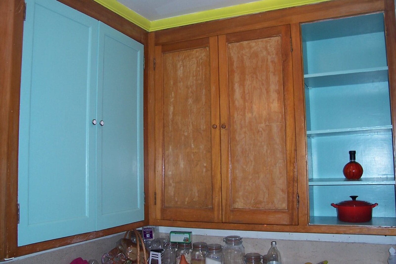 Old wooden kitchen cupboards with one pair of doors freshly painted turquoise beside unpainted ones