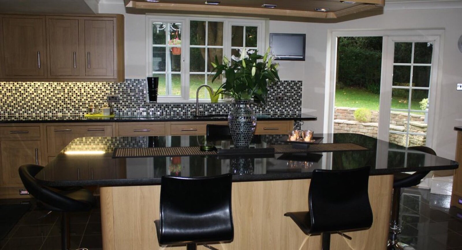 Kitchen island with a polished black worktop and oak units behind
