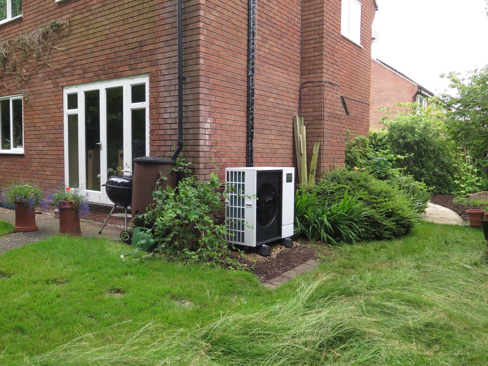 Air source heat pump unit beside a brick house in a garden