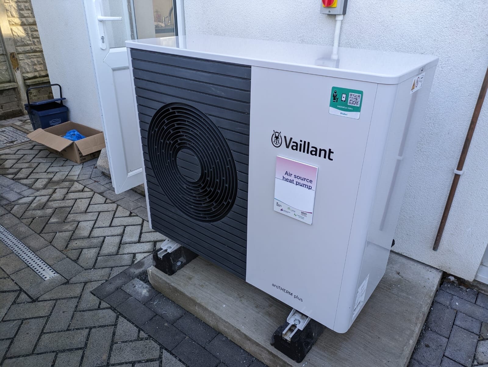 Heat pump outdoor unit on paving at the side of a terraced house