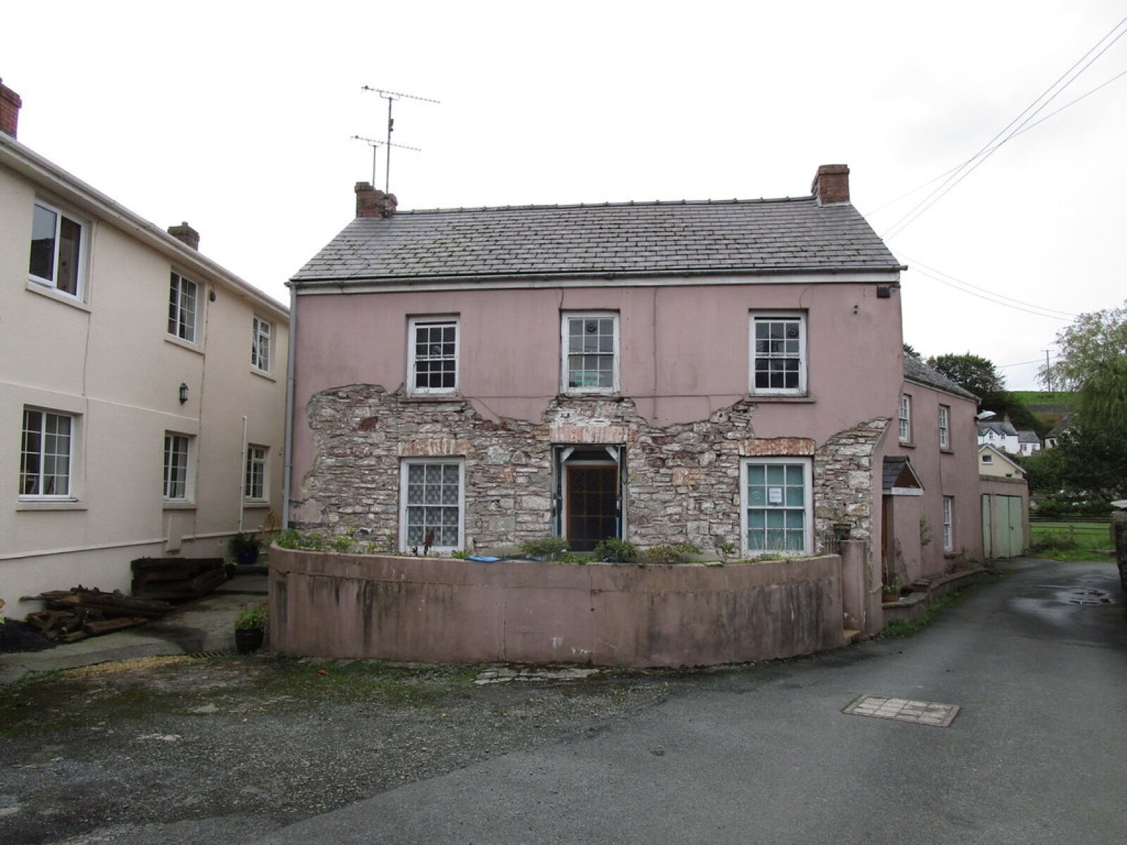 A pink house in Laugharne with render missing from part of its front wall, exposing the stonework beneath