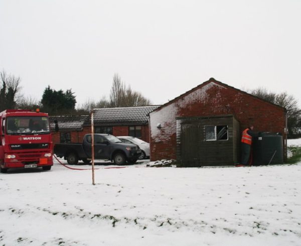 A heating oil tanker parked on a snowy drive while the driver fills a home's oil tank by hose